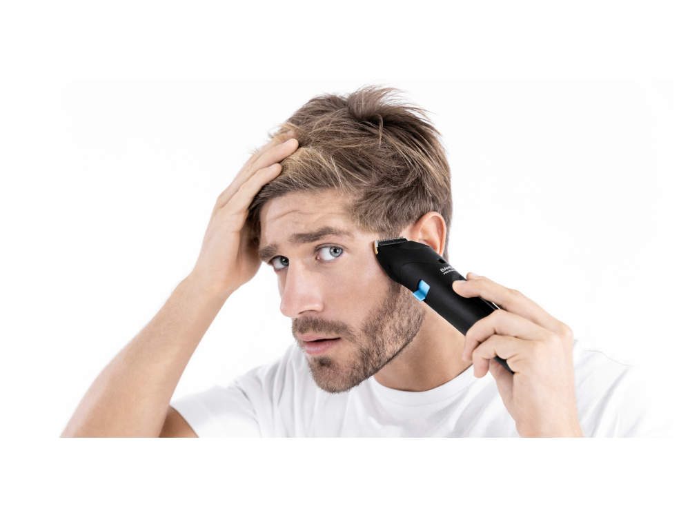 Hombre afeitándose la barba con una recortadora negra, mirándose al espejo, fondo blanco.