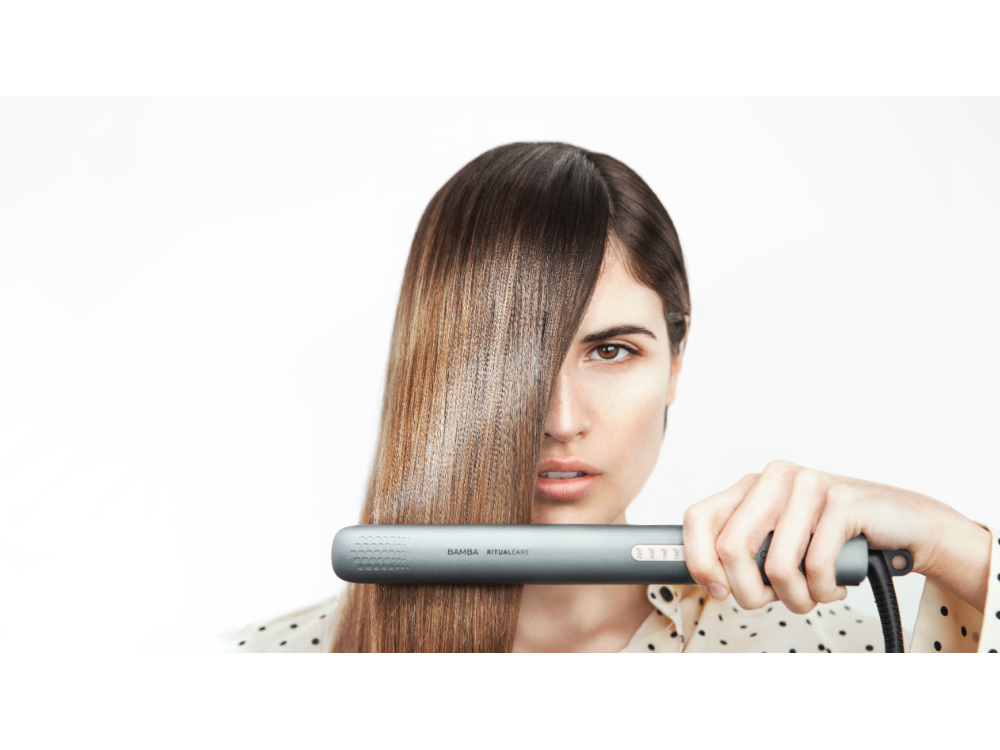 Una mujer sosteniendo una plancha de pelo gris, con cabello liso cubriendo la mitad de su rostro.