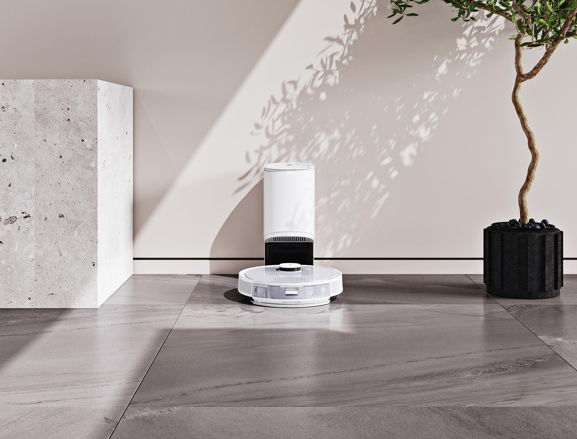Ein weißer Roboter-Staubsauger, eine weiße Basis, ein Baum in einem schwarzen Topf und eine Betonwand.