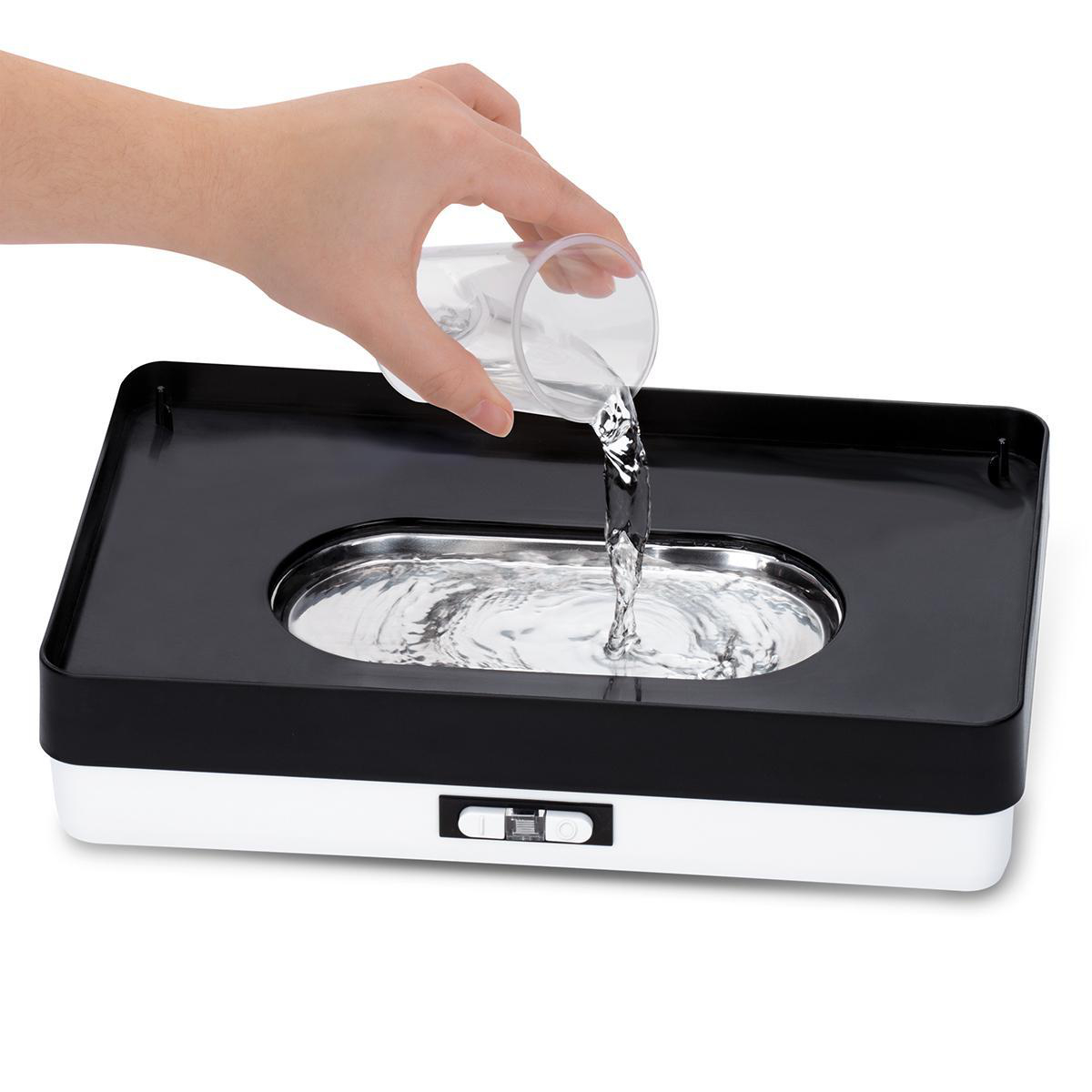 Hand gießt Wasser aus einem Glas in ein schwarz-weißes Reinigungsgerät.