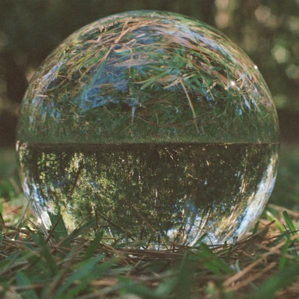 Eine Glaskugel reflektiert grünes Gras und Bäume. Unten Gras, oben die invertierte Szene.