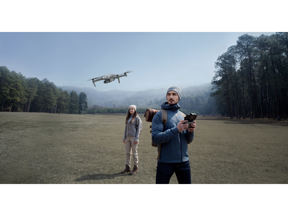 Un dron volando sobre un campo con dos personas, una sosteniendo un controlador.