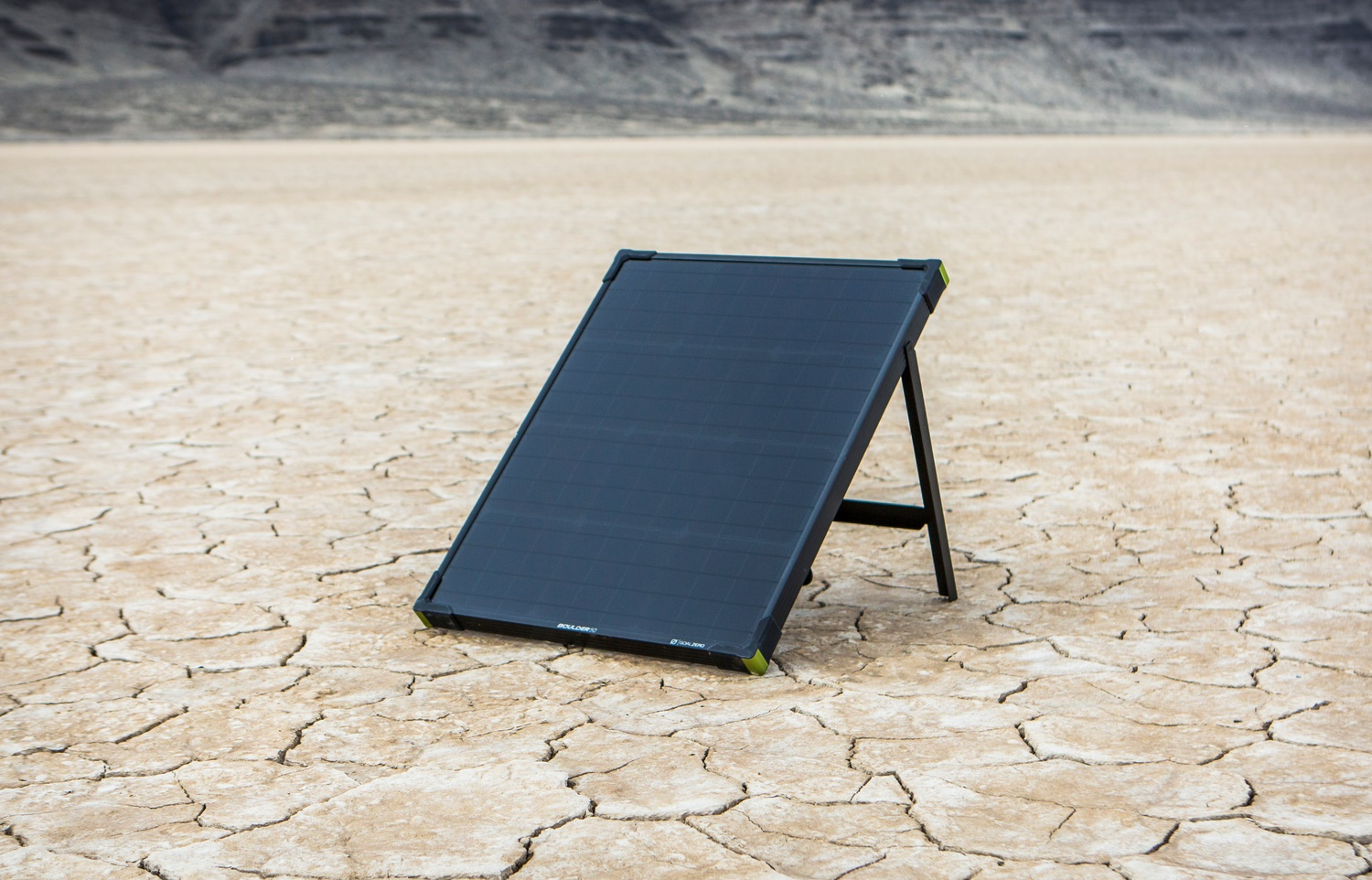 Schwarzes Solarpanel auf einem Ständer vor rissigem, trockenem Erdboden.