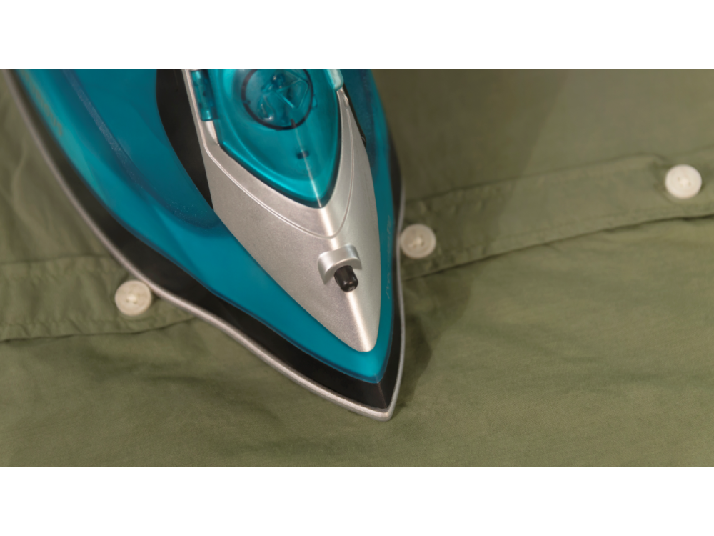 Una plancha planchando una camisa verde. La plancha es verde azulado y plateada, con botones en la camisa.