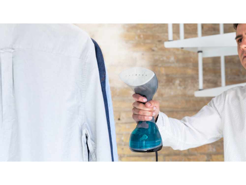 Un hombre plancha una camisa blanca con un vaporizador de mano, camisa en una percha.