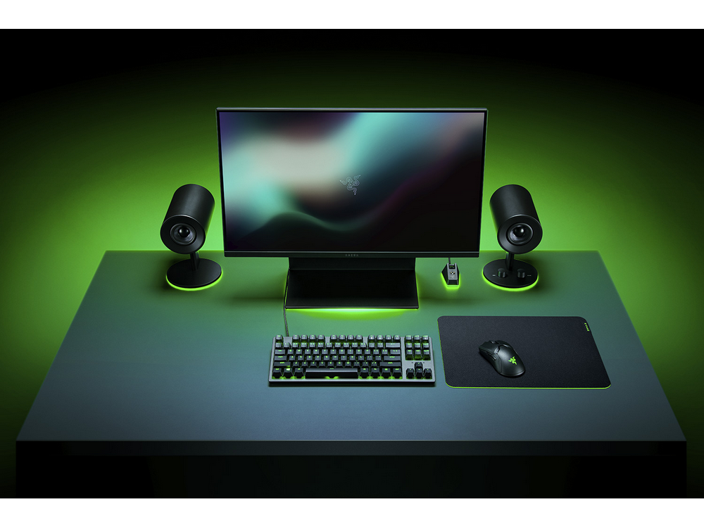 Configuración de juego con monitor, altavoces, teclado, ratón y alfombrilla en escritorio.