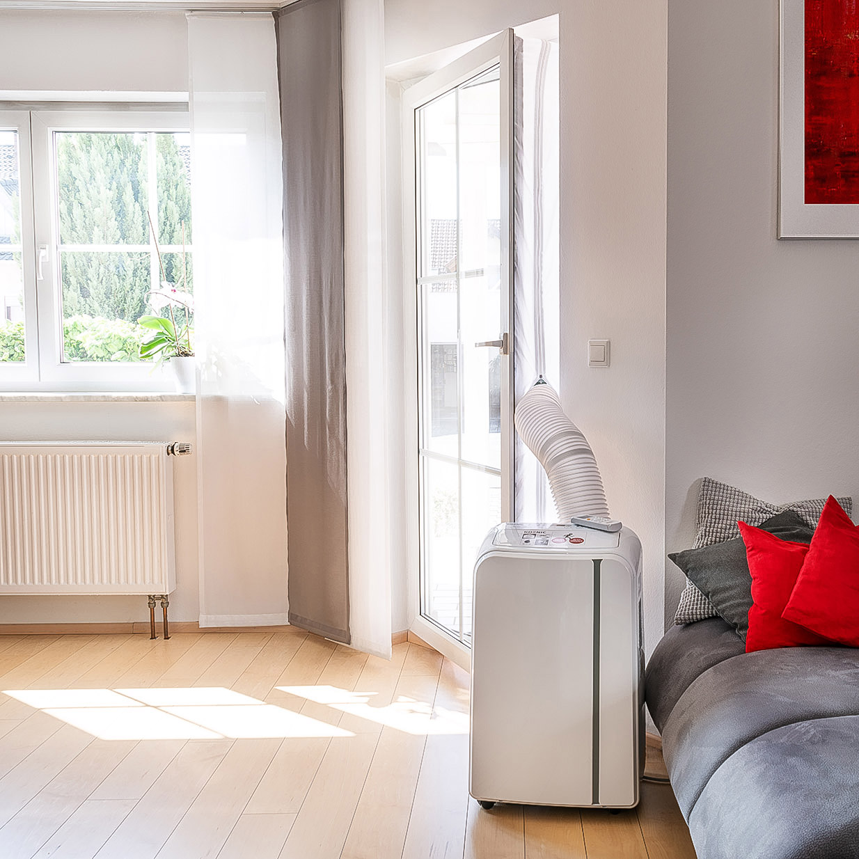 Innenszene mit Klimaanlage am Fenster und Tür. Graues Sofa mit roten Kissen.