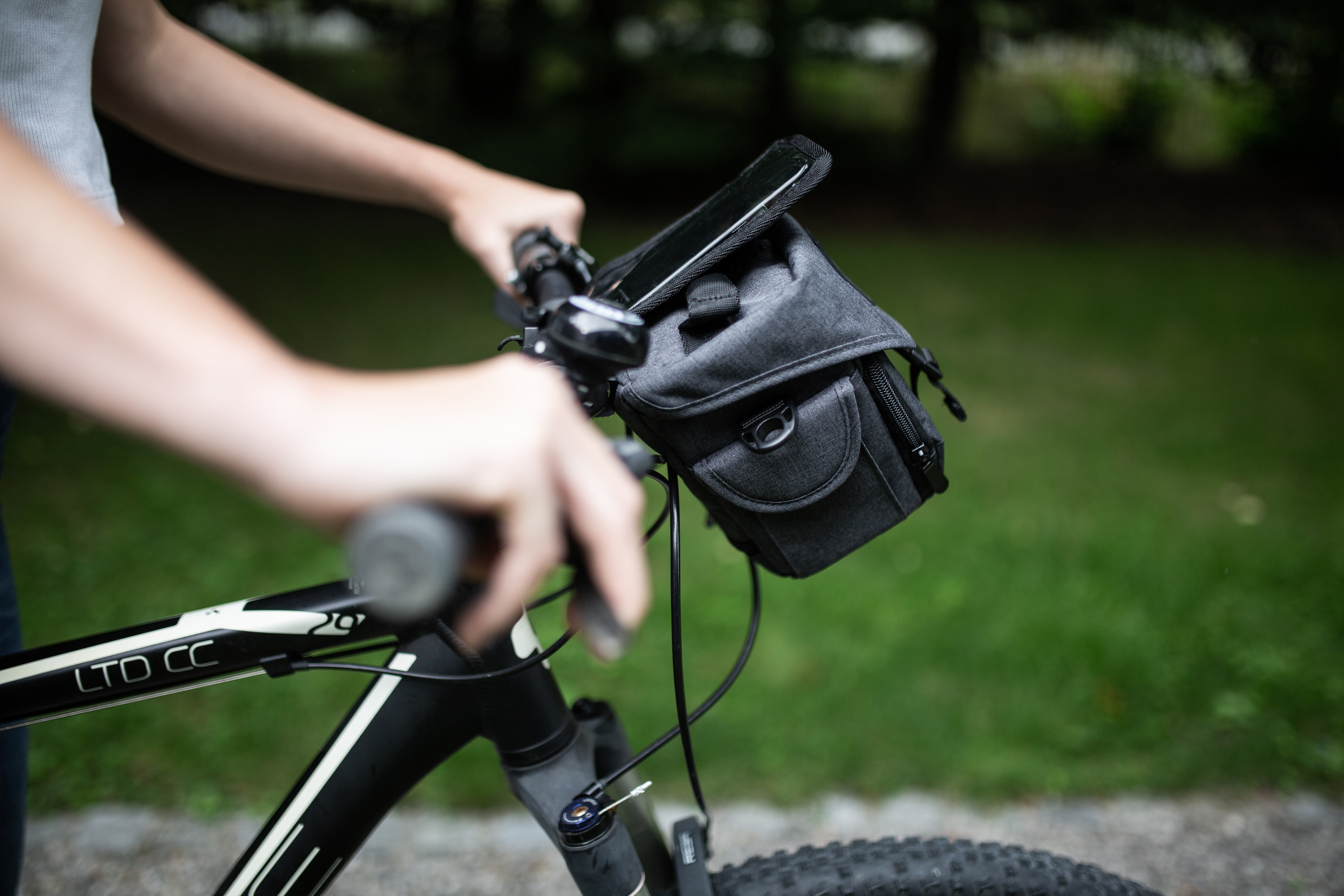 Person hält Fahrradlenker mit einer Telefontasche auf grünem HG.