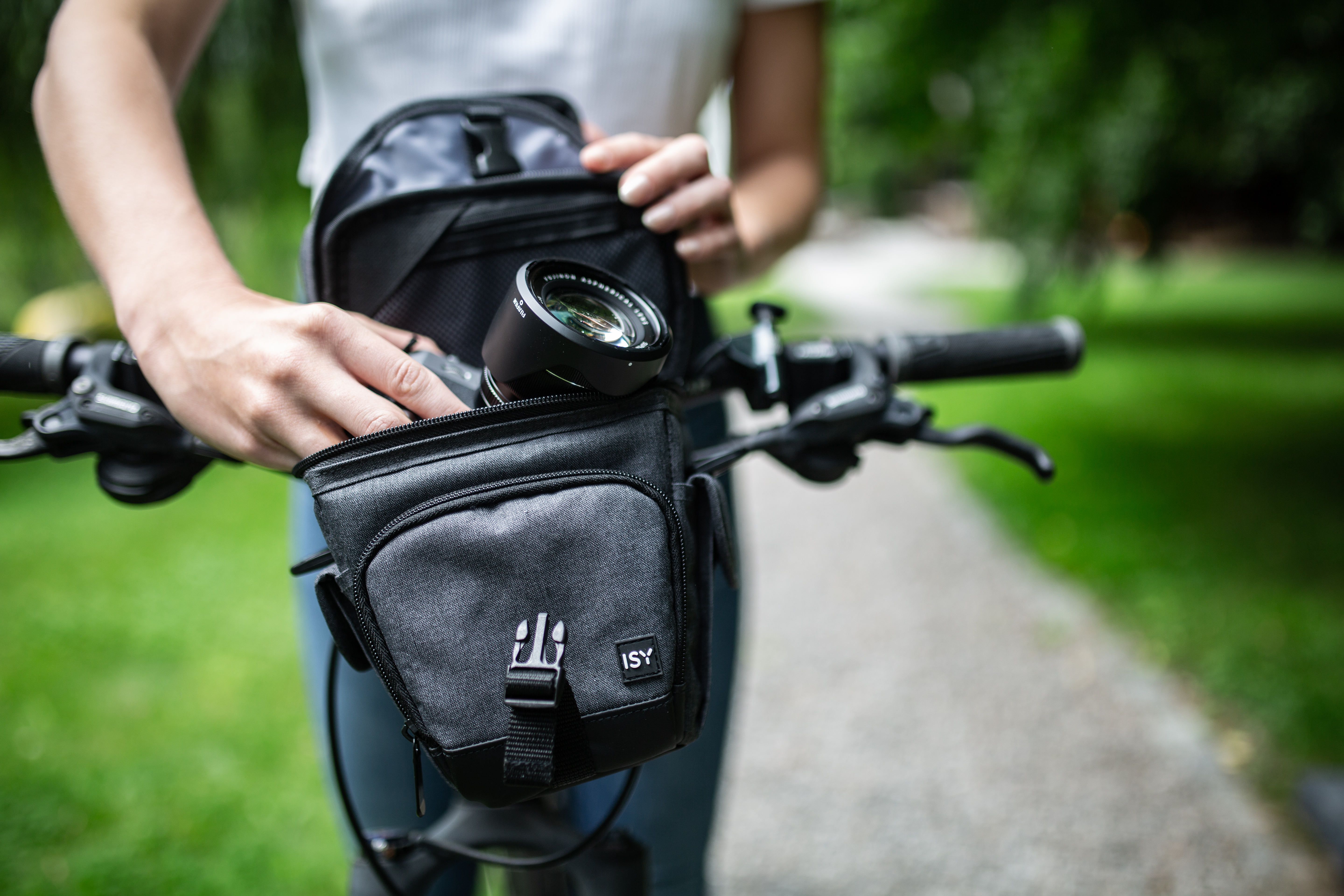 Eine Person legt ein Kameraobjektiv in eine graue Tasche, die an einem Fahrradlenker befestigt ist.