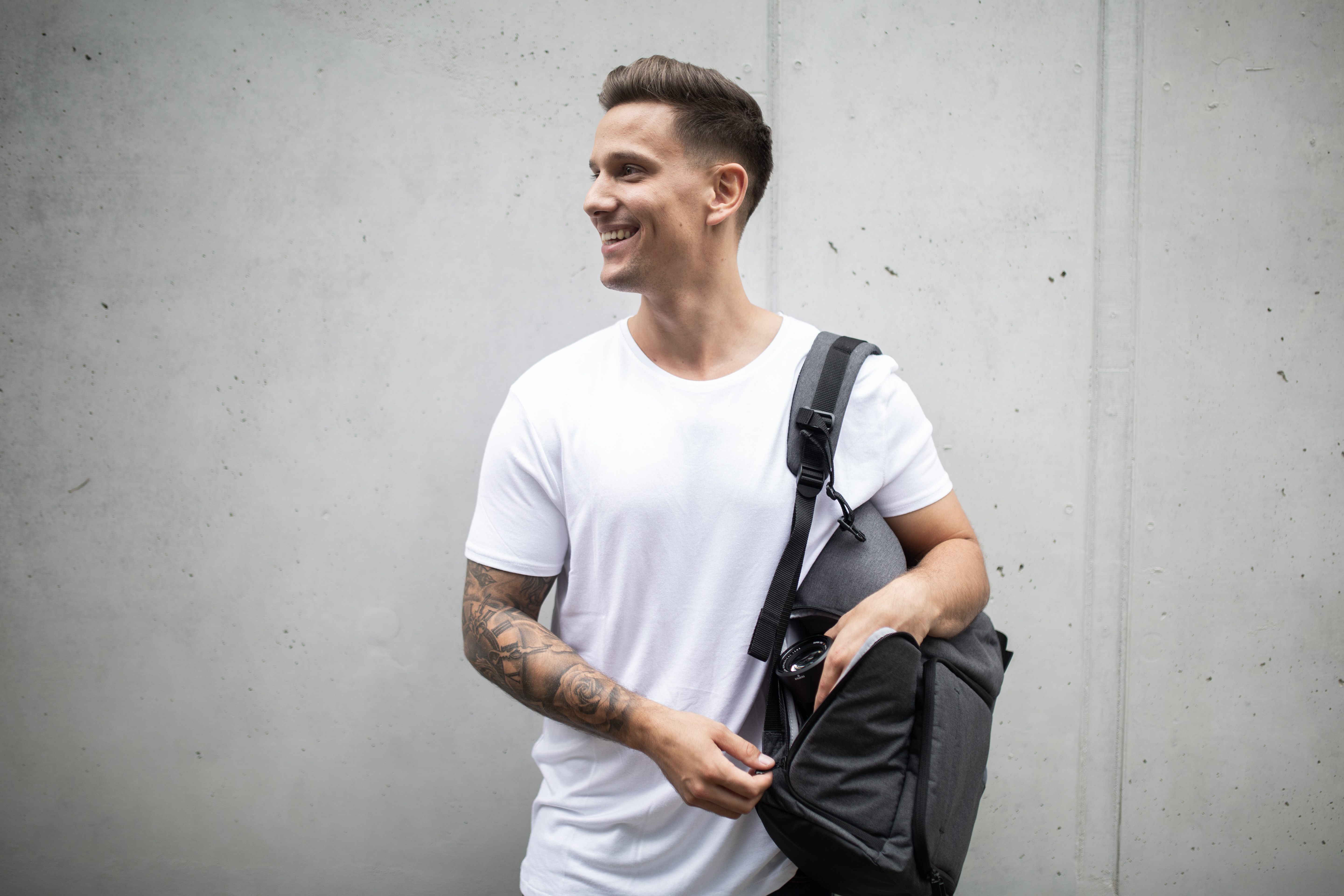 Ein Mann mit Tätowierung auf dem Arm trägt eine Tasche auf der Schulter.