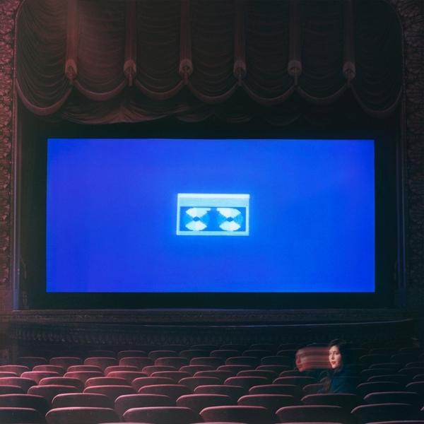 Eine Frau schaut in einem Theater einen Film auf einem großen blauen Bildschirm.