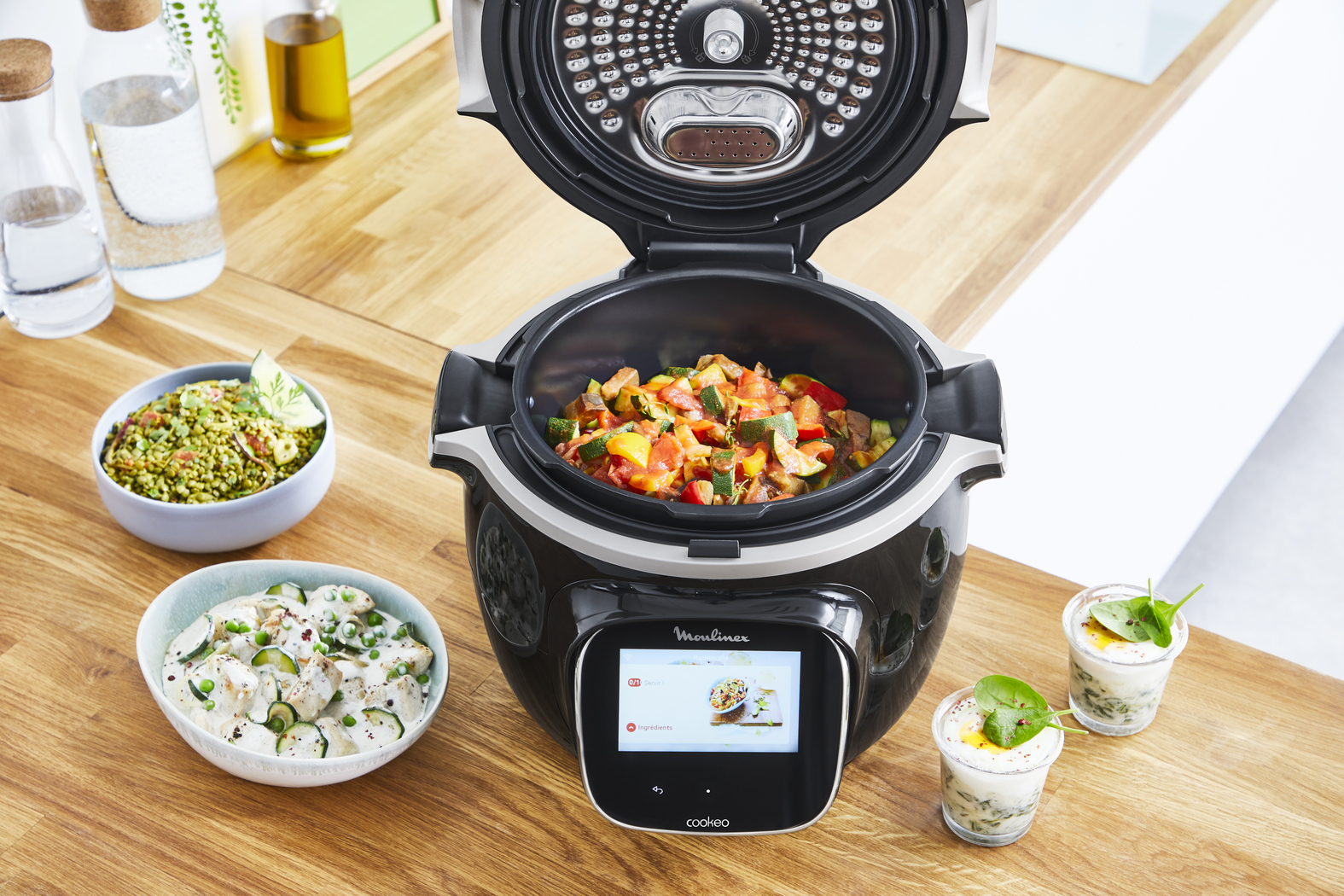 Black Moulinex cooker with an open lid, filled with food, surrounded by bowls and ingredients.