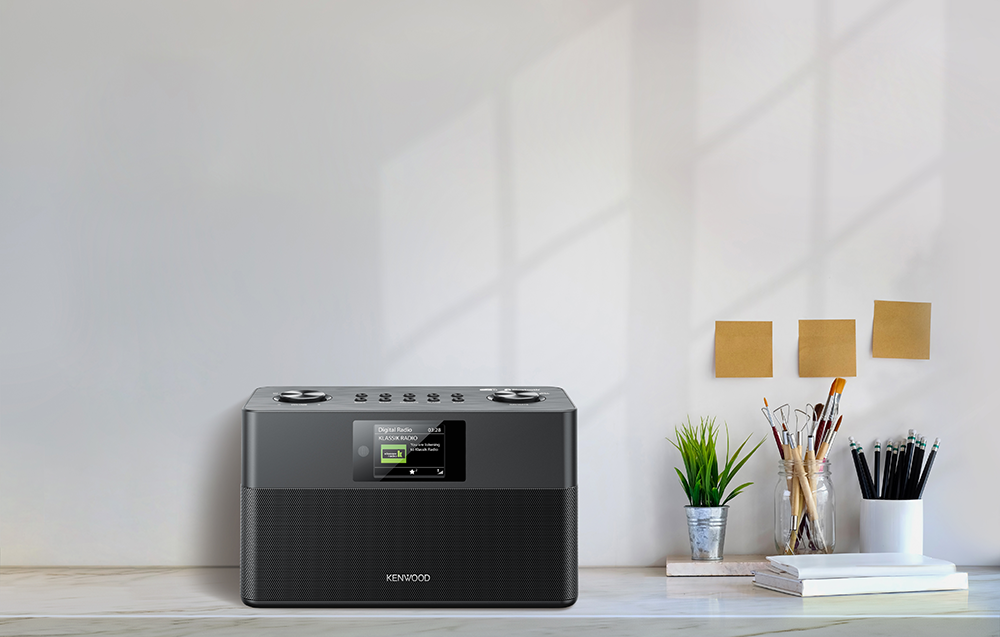 Een Kenwood radio op een bureau met decoraties. Een witte muur op de achtergrond.
