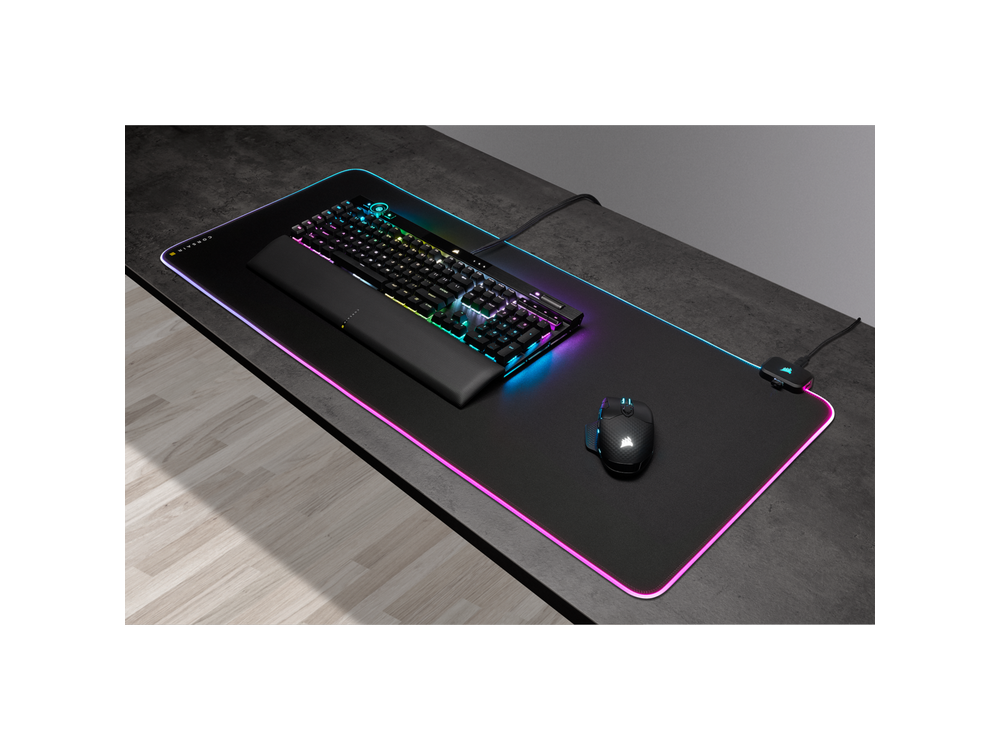 Una configuración de juego con teclado, ratón y alfombrilla con iluminación RGB en un escritorio negro.