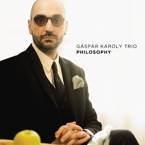 Férfi öltönyben, szemüvegben és nyakkendőben. Szöveg: Gáspár Károly Trio Philosophy.