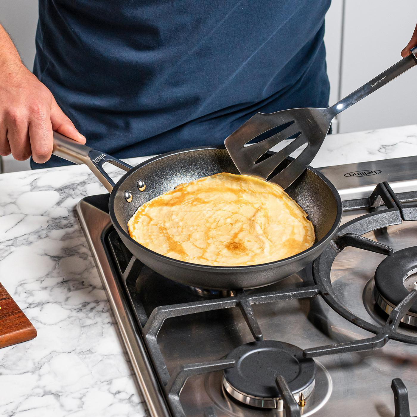 Person bereitet einen Crêpe in einer Pfanne auf einem Gasherd zu.