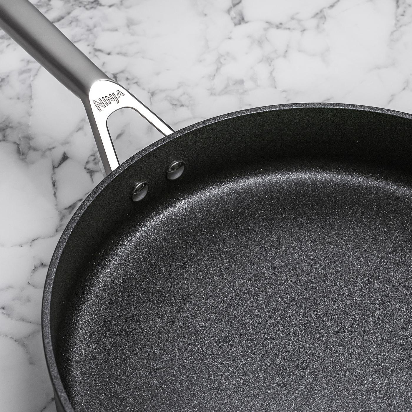 Schwarze Bratpfanne mit silbernem Griff, auf einer Marmoroberfläche stehend.