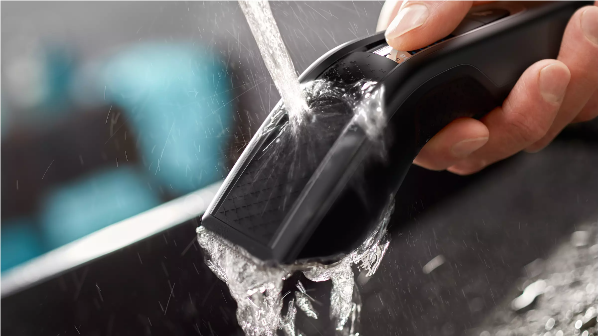 Water is running over a black electric shaver. A hand holds the shaver.