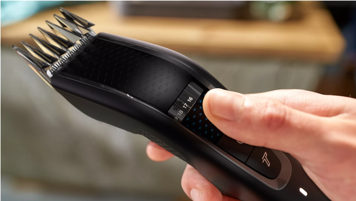 Hand using clippers to adjust the blade length on a black hair clipper.