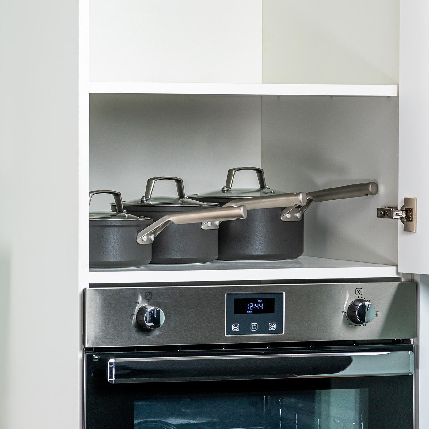 Küchenschrank mit Töpfen und Pfannen darin. Ofen ist unter dem Regal sichtbar.