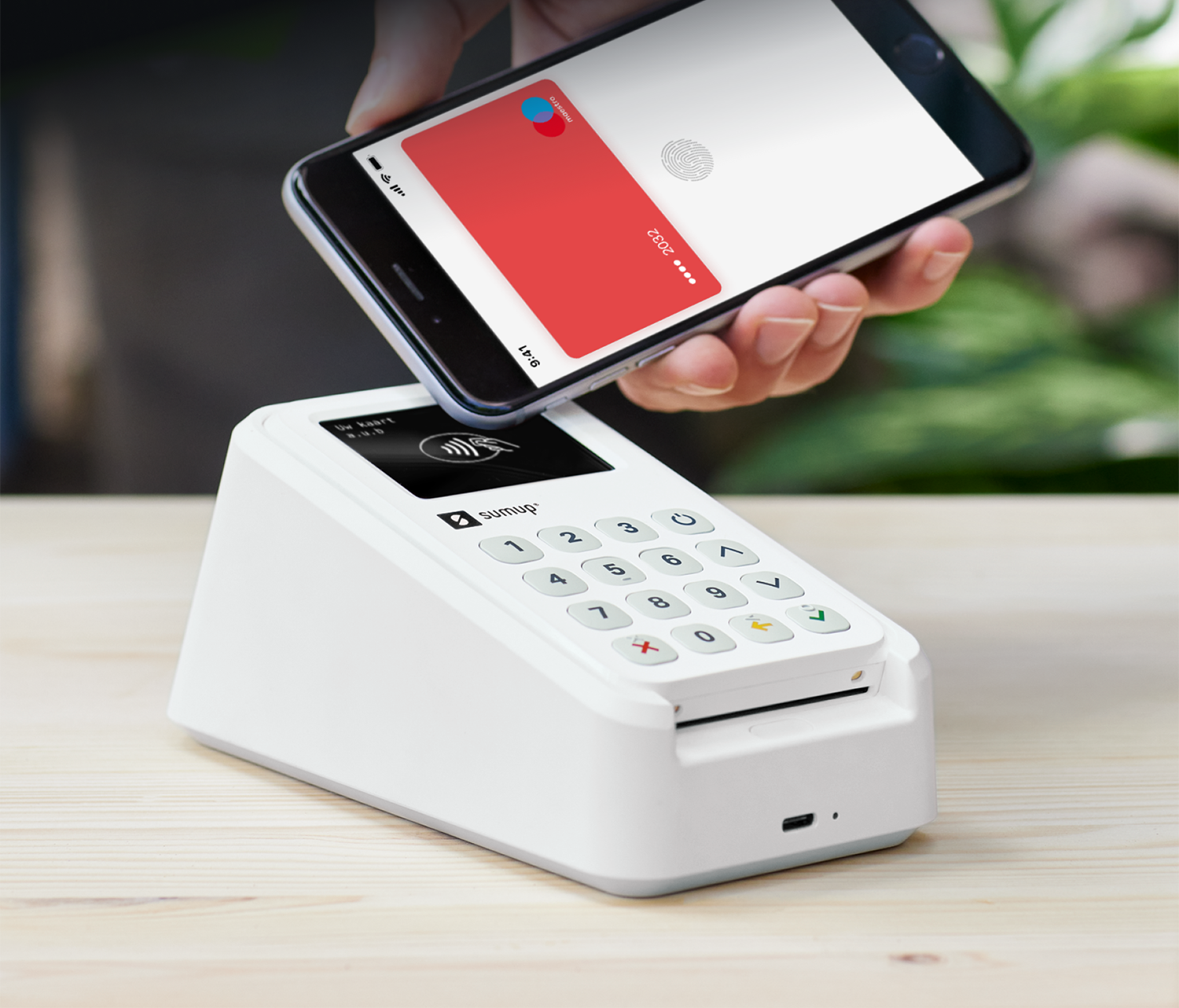 A phone being placed on a white payment terminal, with a red card and a fingerprint.