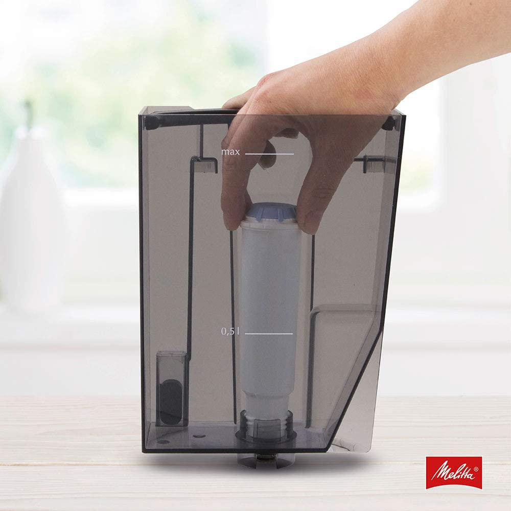 Hand hält Wasserfilter in transparentem Kaffeemaschinenbehälter.