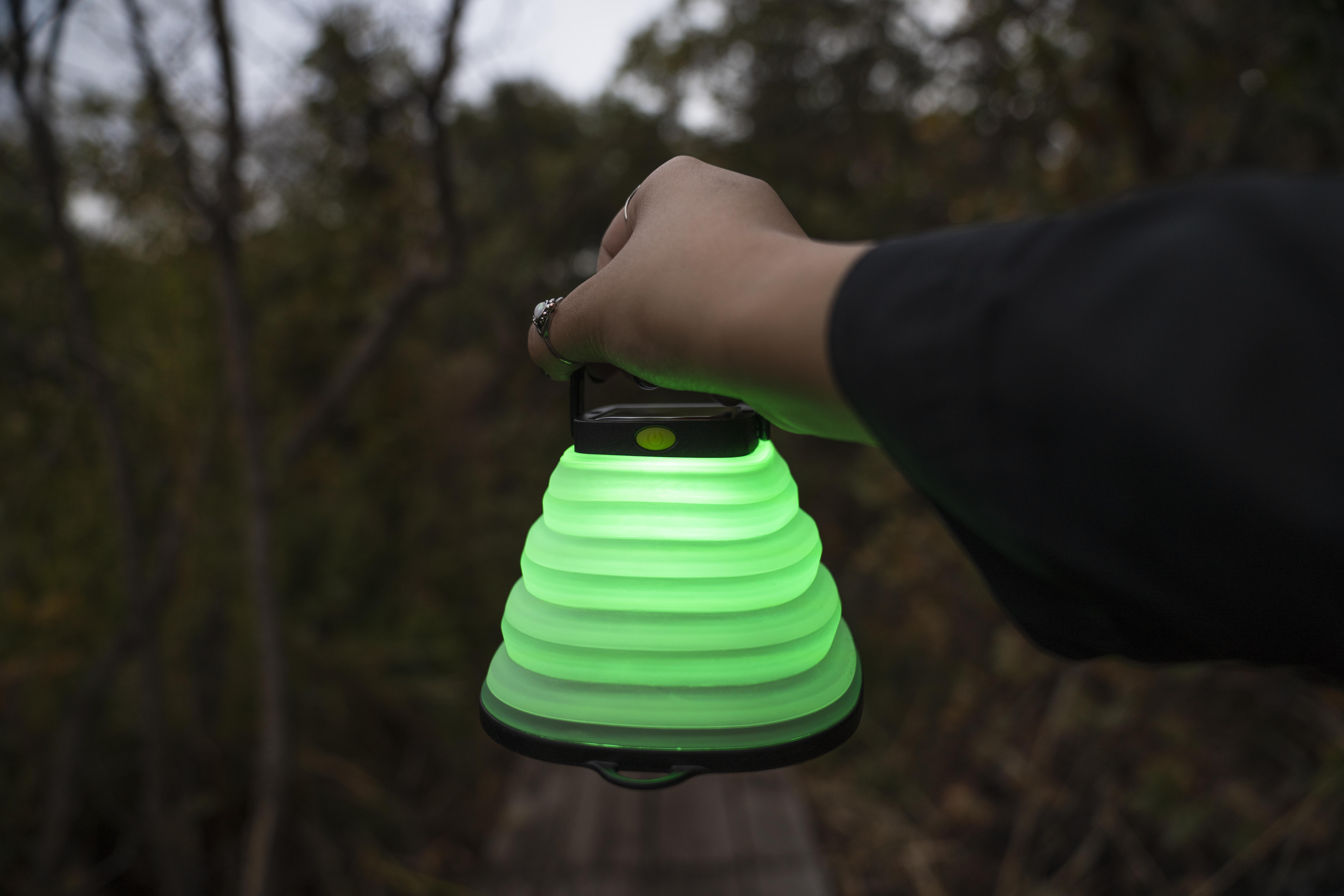 Hand hält eine grüne Laterne im Wald, die hell leuchtet.