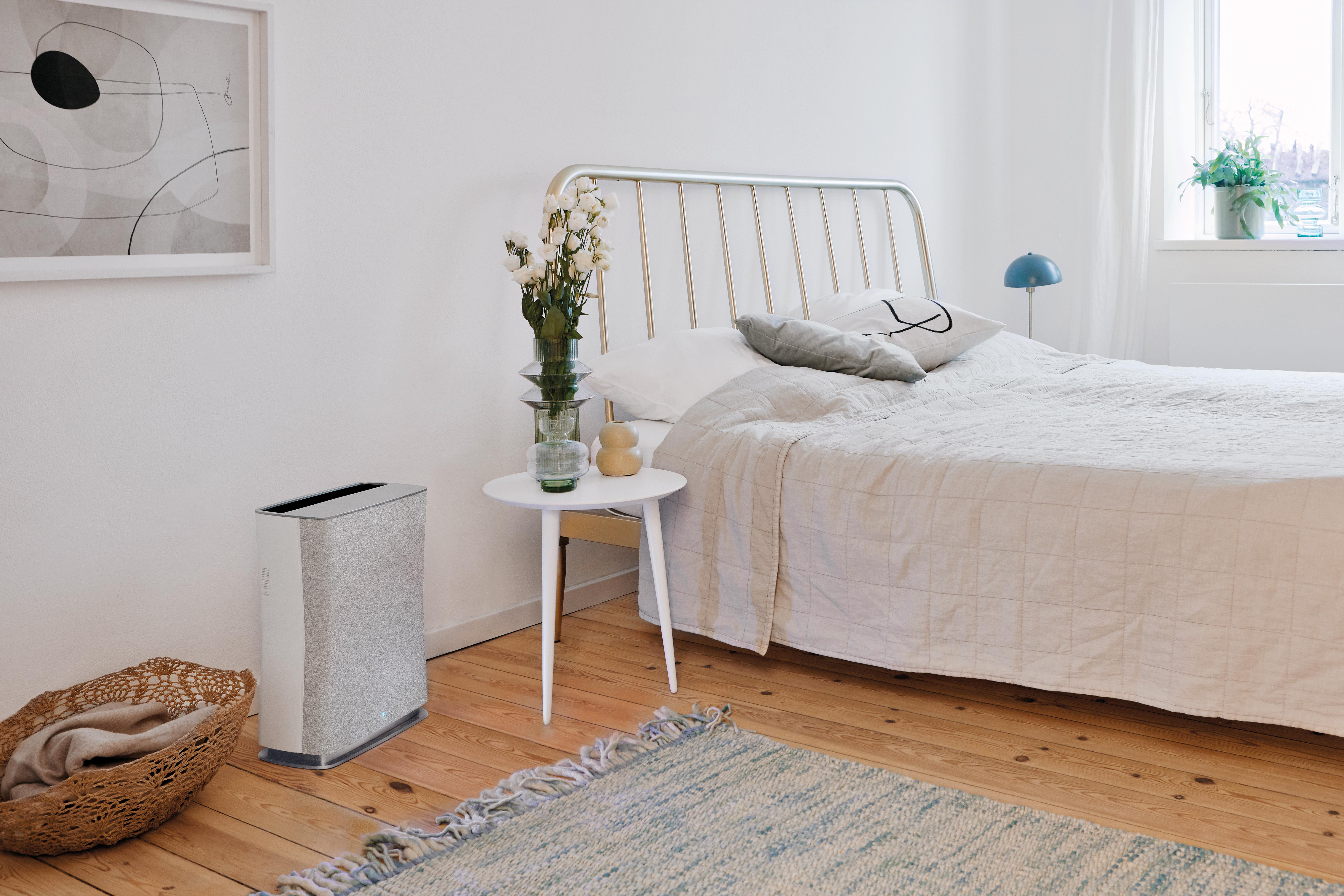 Schlafzimmer mit Bett, Tisch, Blumen, Luftreiniger und Teppich.