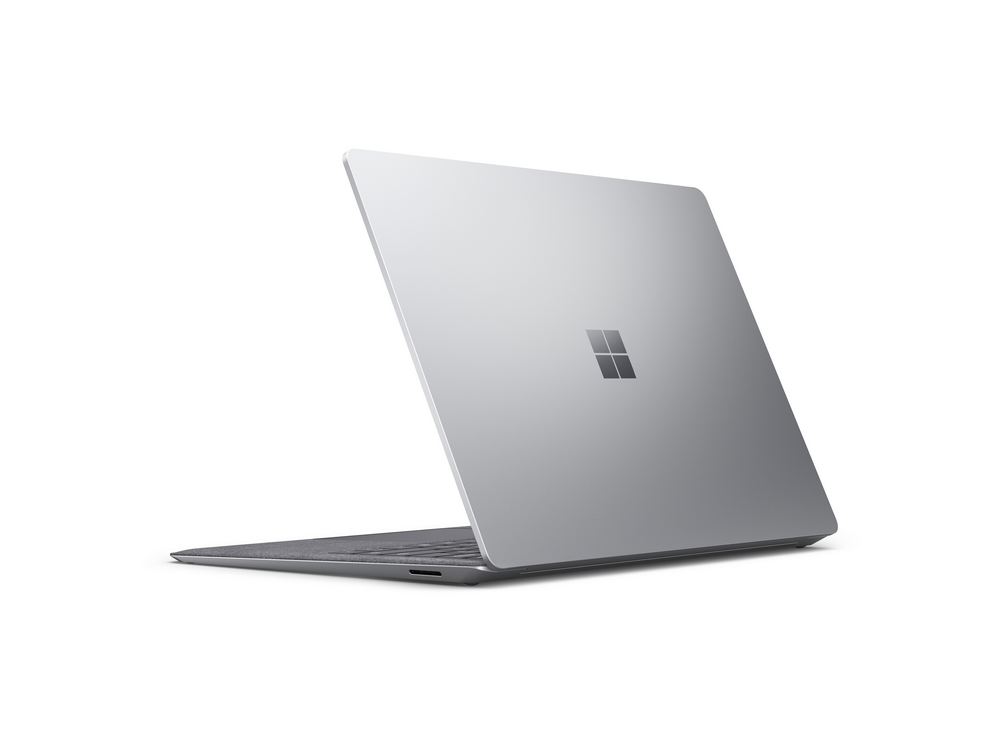 Laptop plateado, vista trasera, con tapa cerrada, sobre superficie blanca. Logo Microsoft visible.