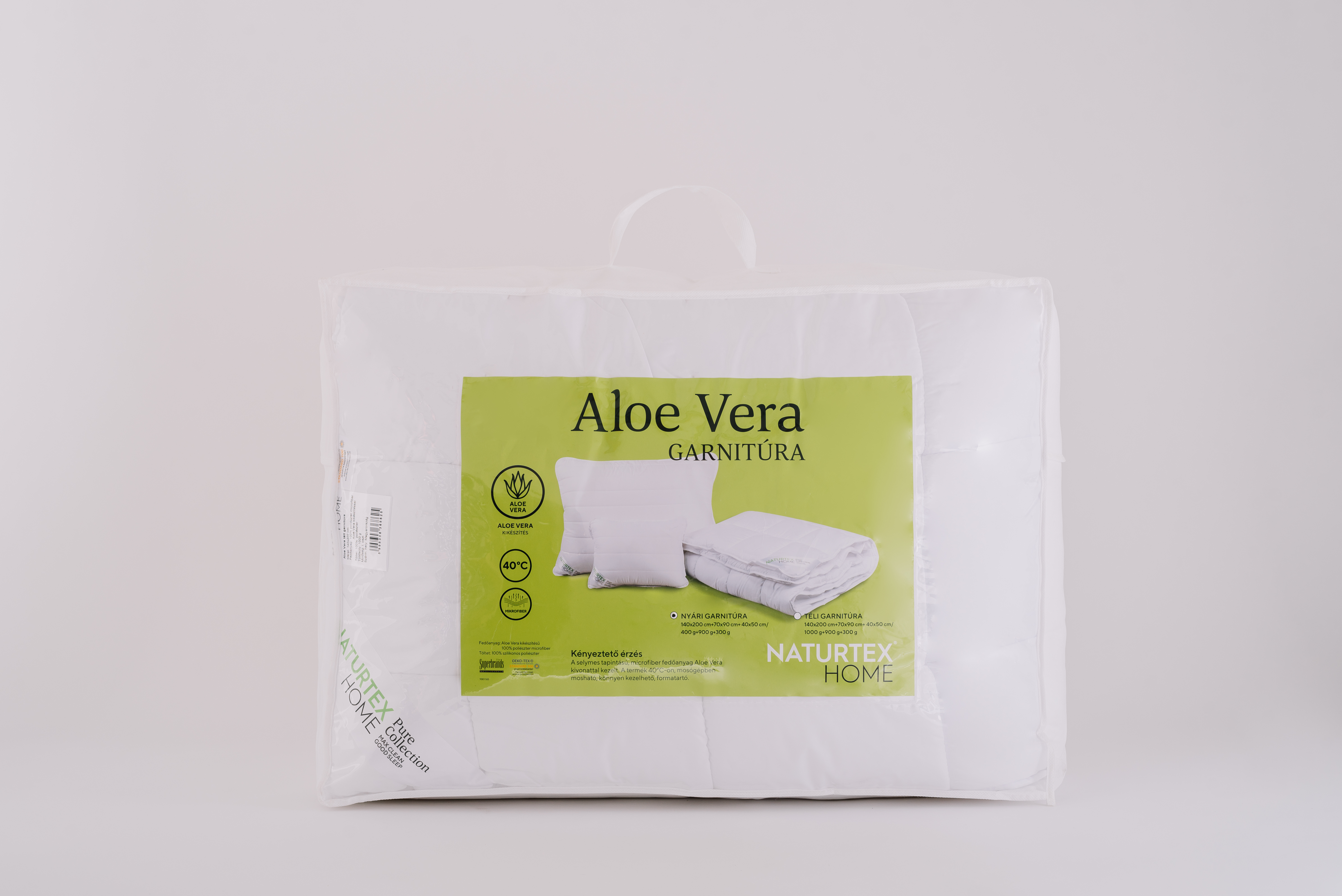 Fehér csomag párnával és takaróval, 'Aloe Vera Garnitura' logóval. Fehér háttér, átlátszó műanyag.