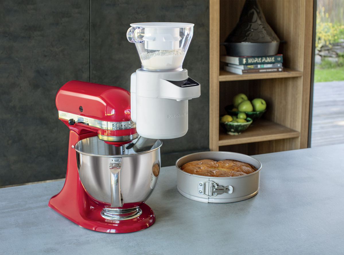 Ein roter KitchenAid-Mixer mit einer angebrachten weißen Getreidemühle und einem Kuchen.