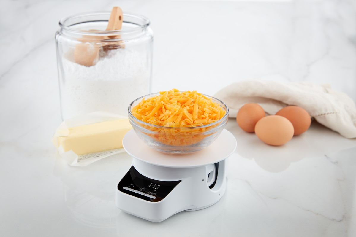Zutaten auf einer weißen Waage: Mehl, Butter, Käse und Eier.