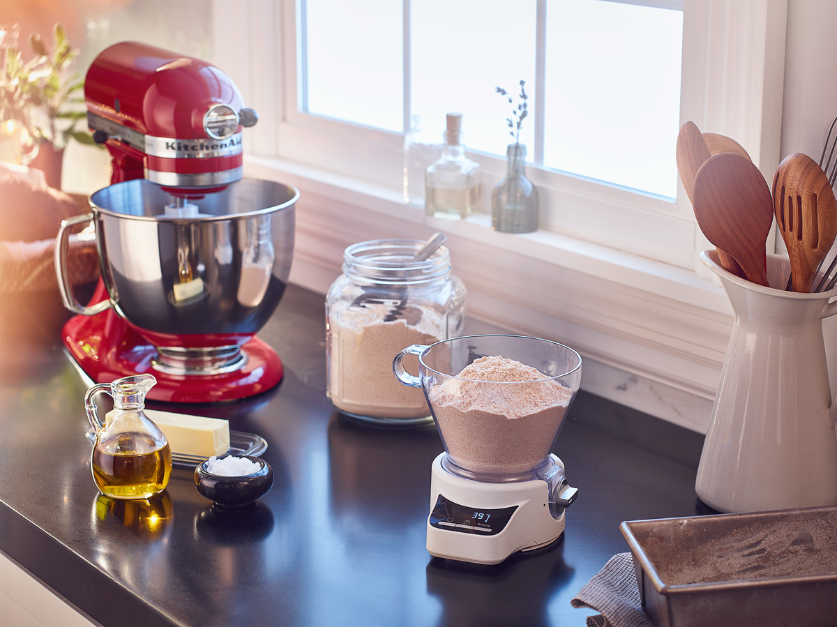 Küchenszene mit roter KitchenAid-Mixer, Zutaten und Messbecher. Fenster und Holzlöffel sind sichtbar.