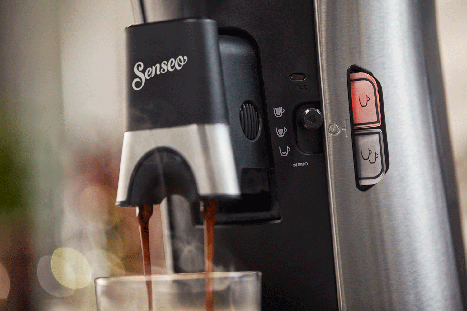 Close-up of a black and silver coffee machine dispensing coffee into a glass.