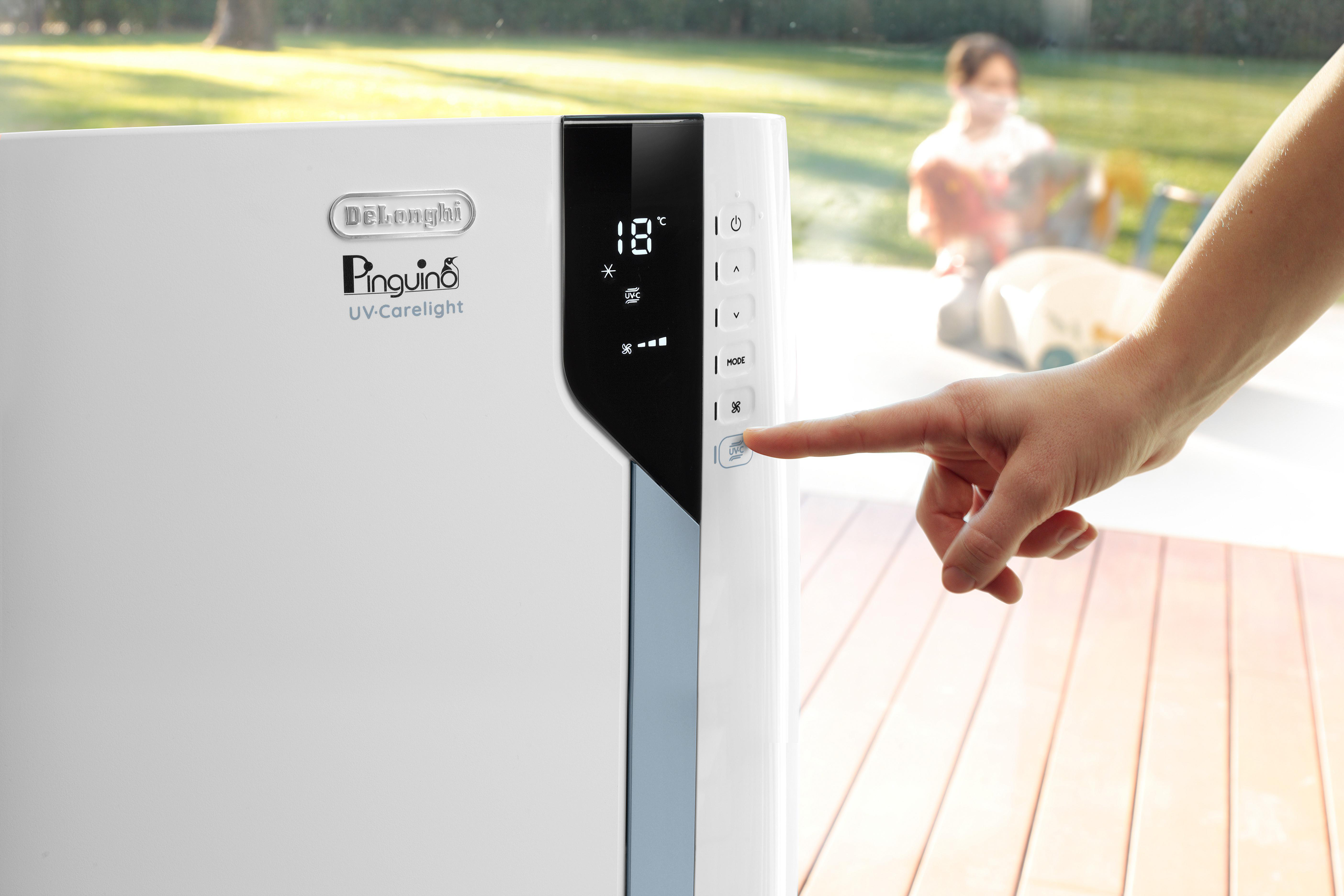 Weißer DeLonghi Klimaanlage, Finger drückt eine Taste.