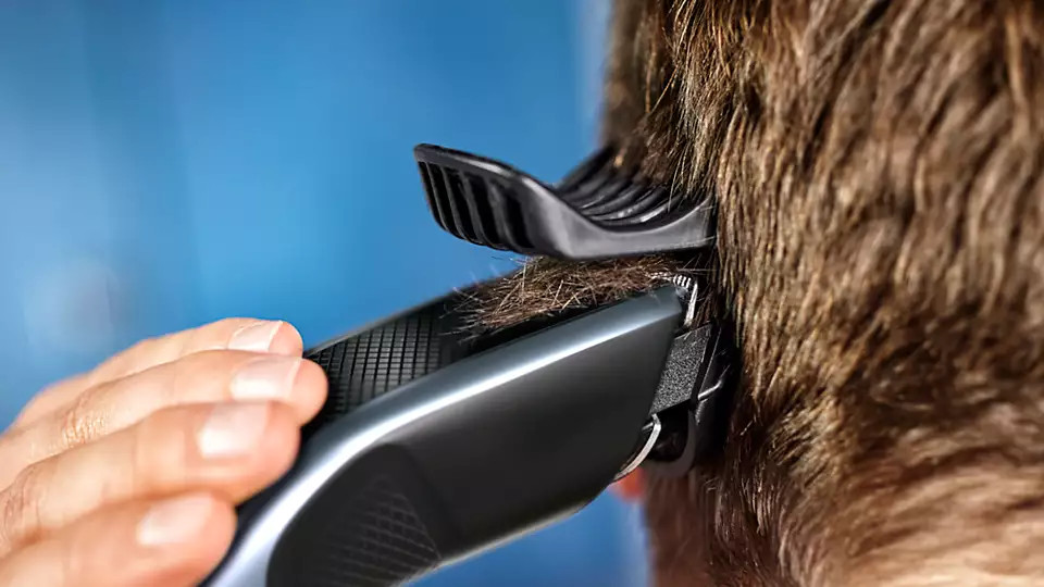 A person using a hair clipper to cut hair on the back of someone's head.