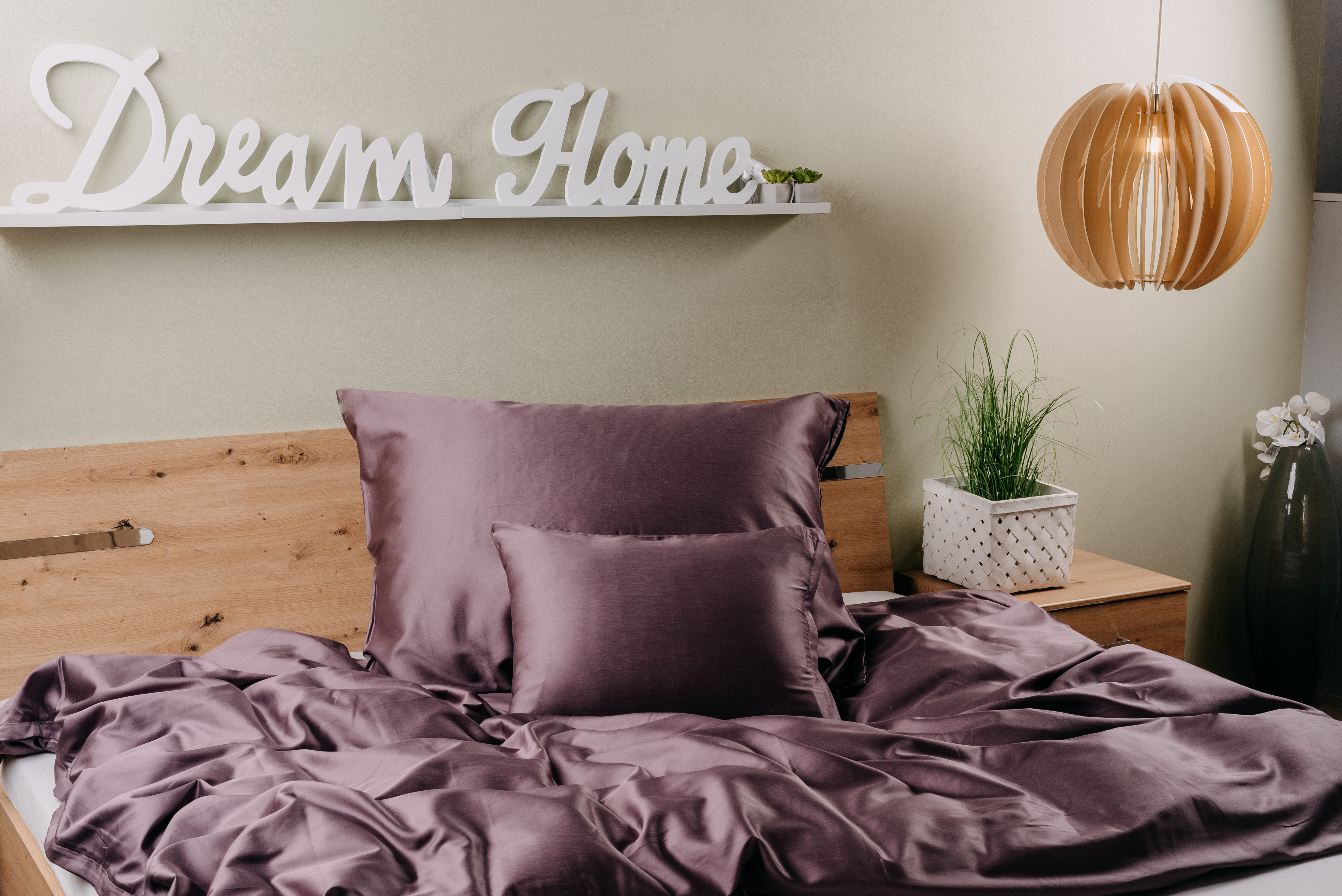 Egy hálószoba, lila ágyneművel borított ággyal és egy 'Dream Home' táblával a falon.