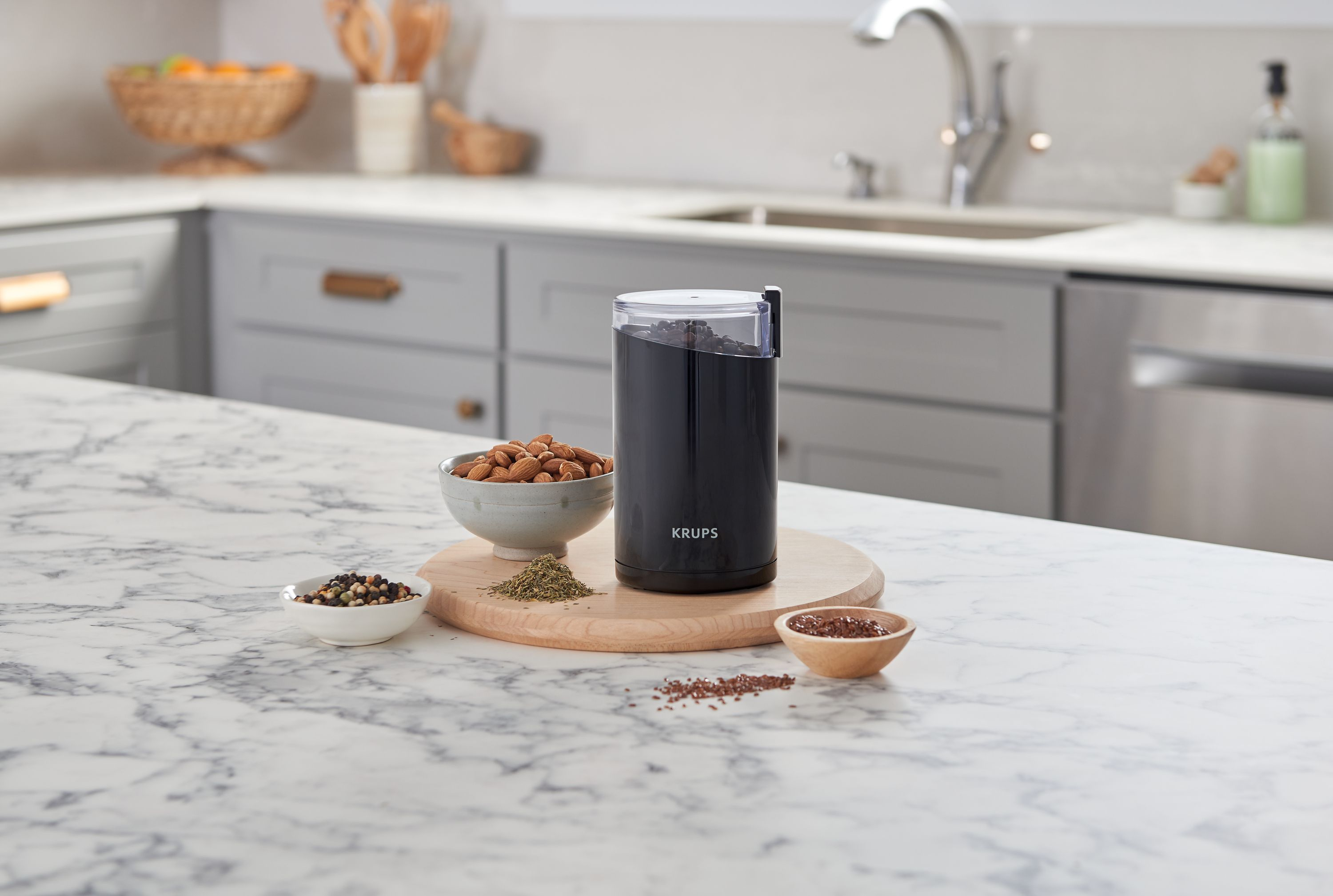 Schwarze Krups Kaffeemühle auf einem Holzbrett mit Gewürzen und Mandeln auf einer Marmorarbeitsplatte.