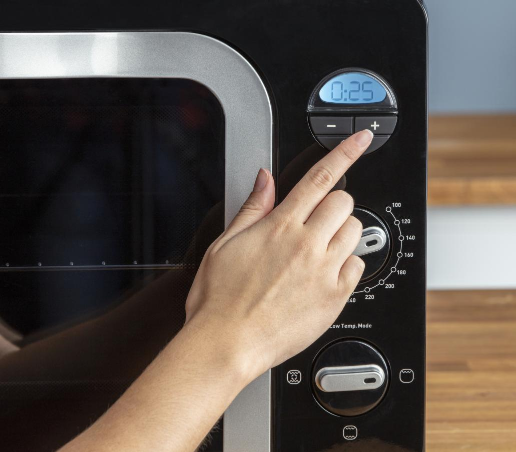 Close-up of a hand adjusting the timer on a black oven with a digital display.