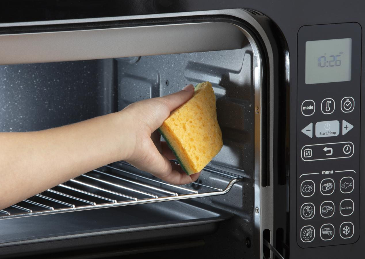 Hand cleaning the inside of a black Moulinex oven with a sponge.
