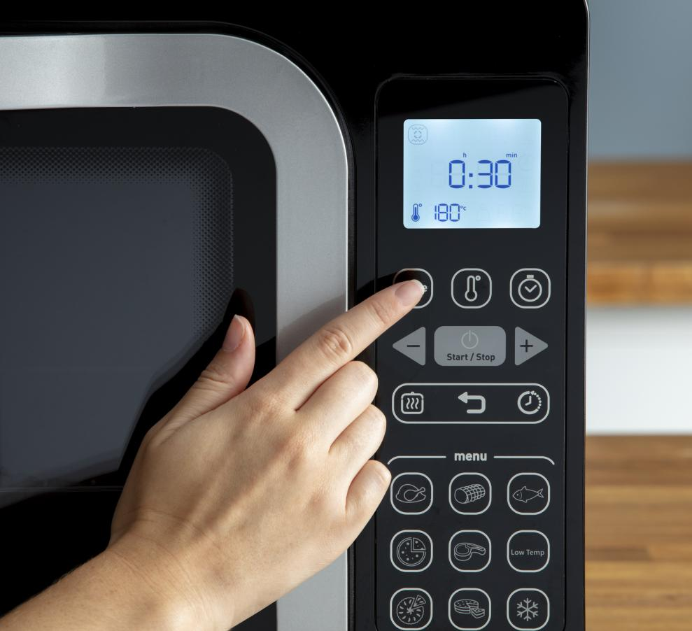 A hand pressing a button on a microwave control panel, showing time and temp.