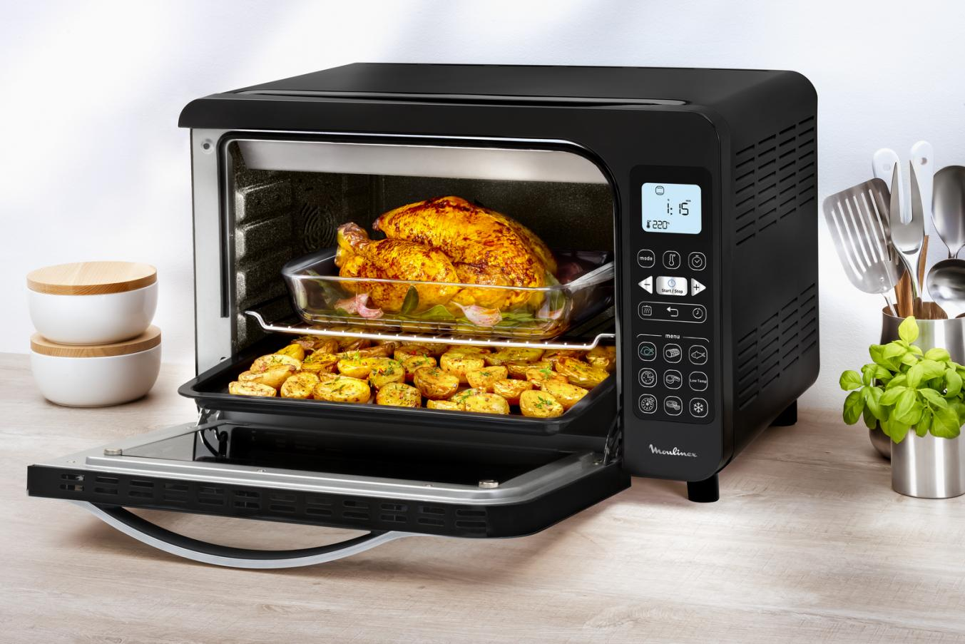 Black Moulinex oven with a roasted chicken and potatoes inside.