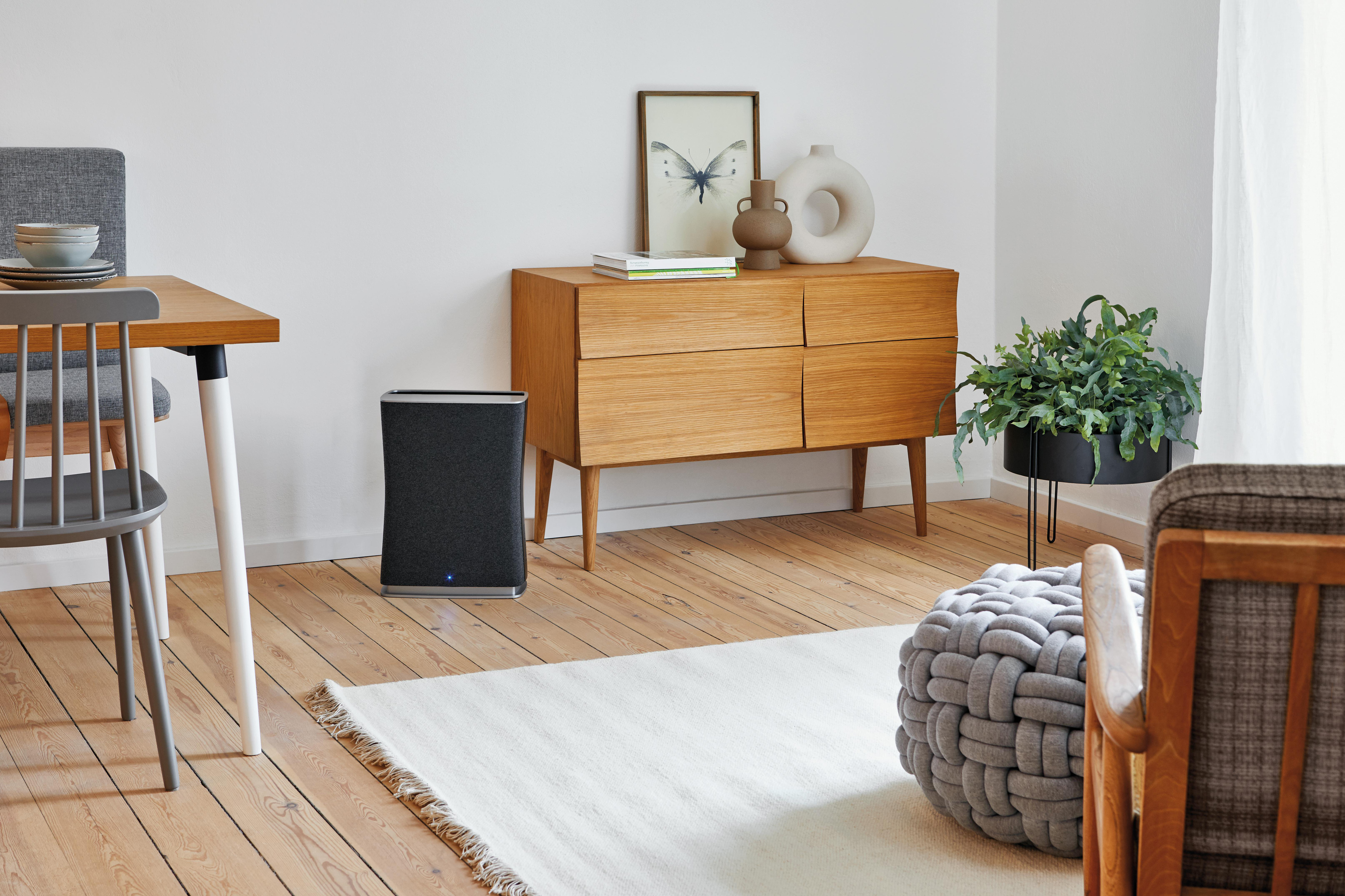 Ein Wohnzimmer mit Holzschrank, Tisch und Teppich. Ein schwarzer Luftreiniger ist vorhanden.