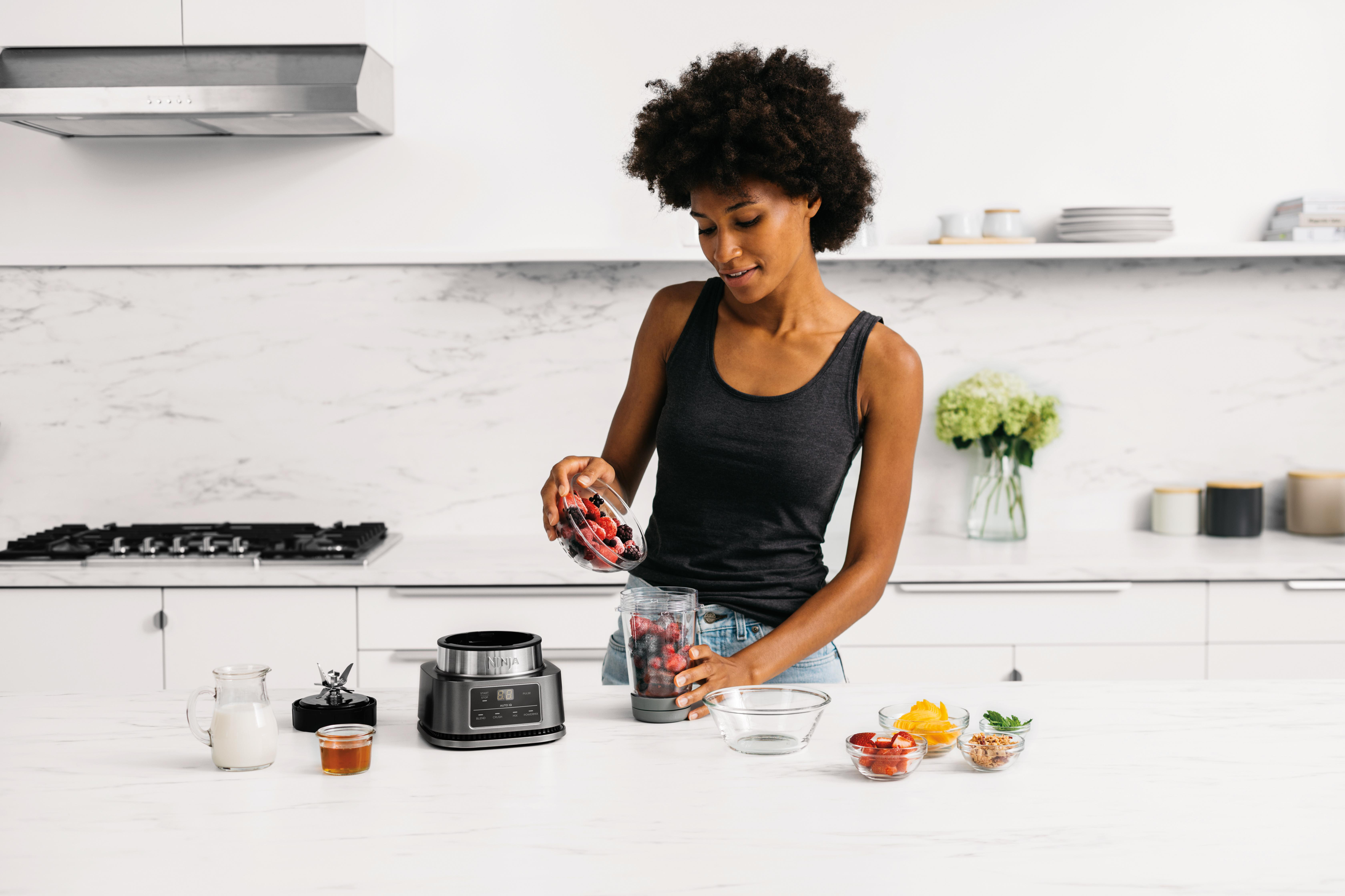 Frau fügt Beeren in einen Mixer, Küchenartikel auf der Theke.