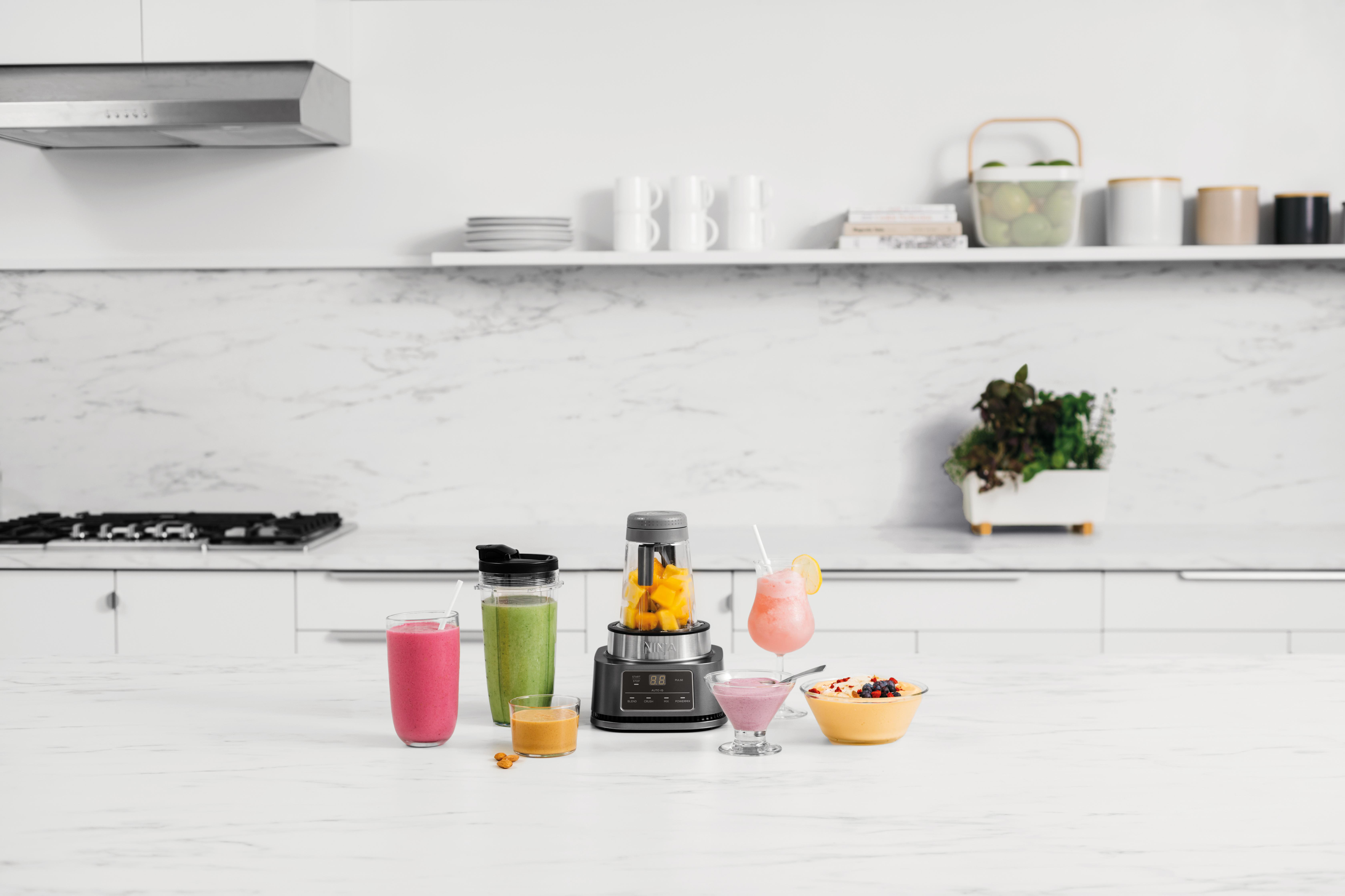 Küchentheke mit einem Mixer, Smoothies und Obstschalen.