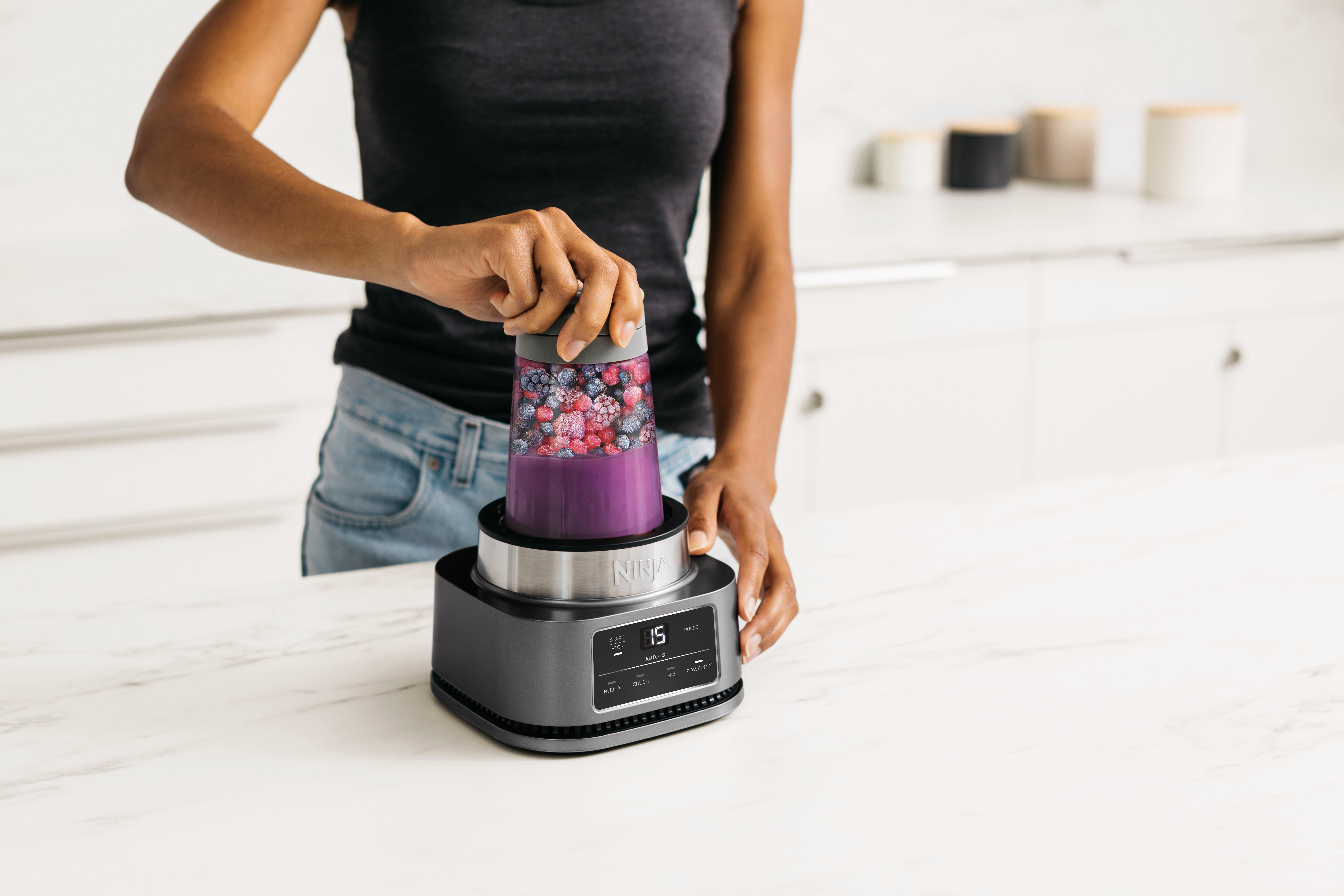 Eine Frau benutzt einen Mixer. Der Mixer ist mit Beeren und einer lila Flüssigkeit gefüllt.