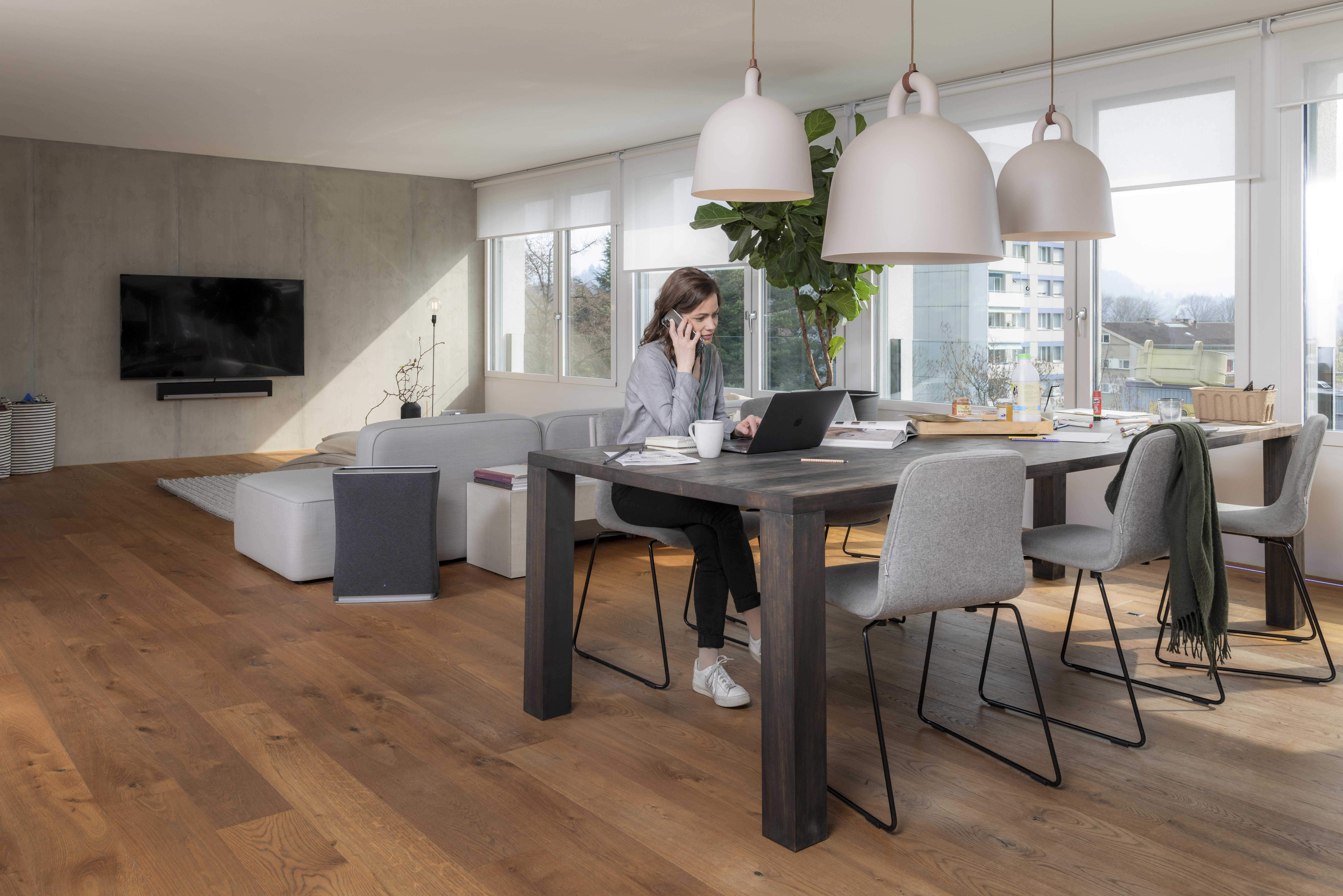 Frau telefoniert und arbeitet am Laptop am Holztisch im Wohnzimmer.