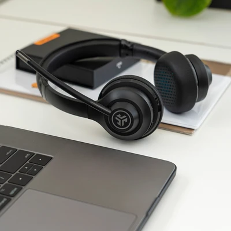 Cuffie nere con microfono, appoggiate su un laptop e un quaderno.