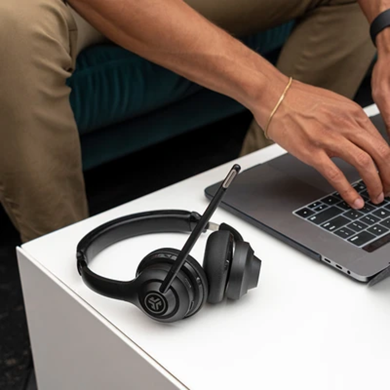 Persona che usa un laptop con cuffie, seduta su un divano.