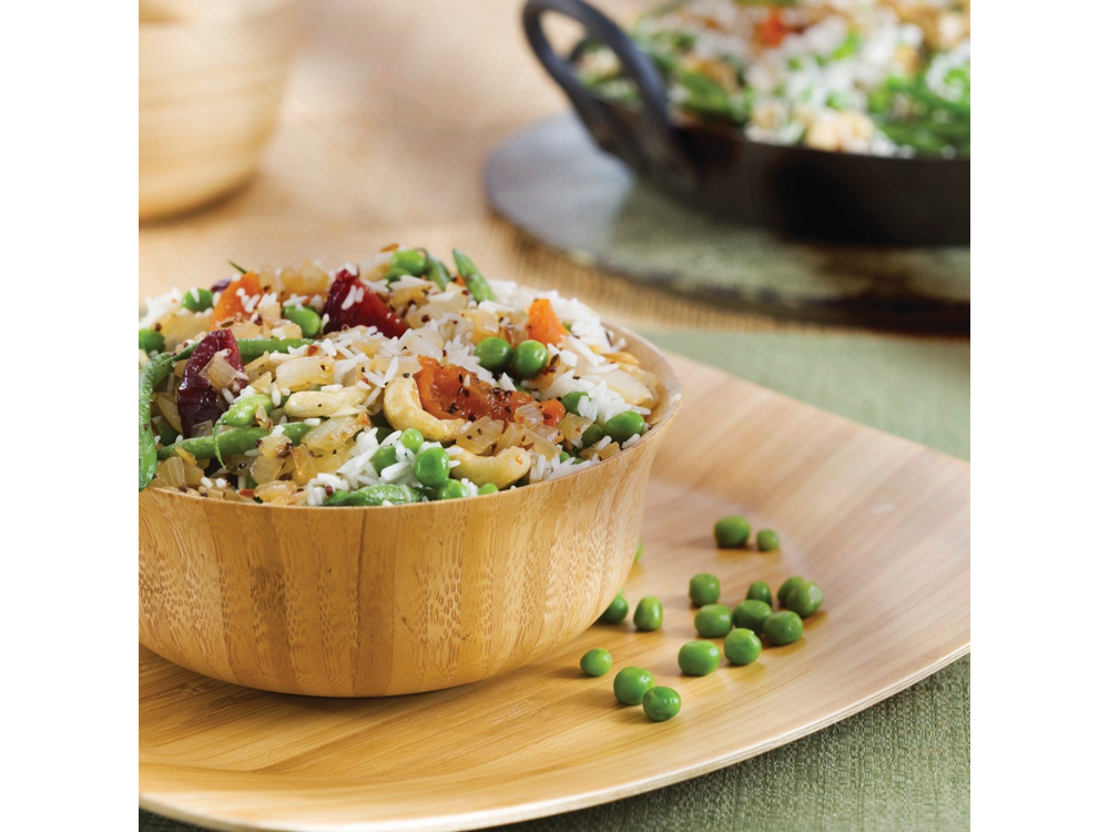 Un cuenco de arroz y verduras en una tabla de madera, más arroz al fondo.